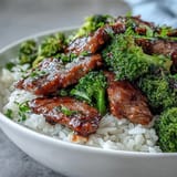 A sizzling skillet of Beef and Broccoli Bowl tossed in glossy soy-ginger sauce, served beside a mound of jasmine rice.