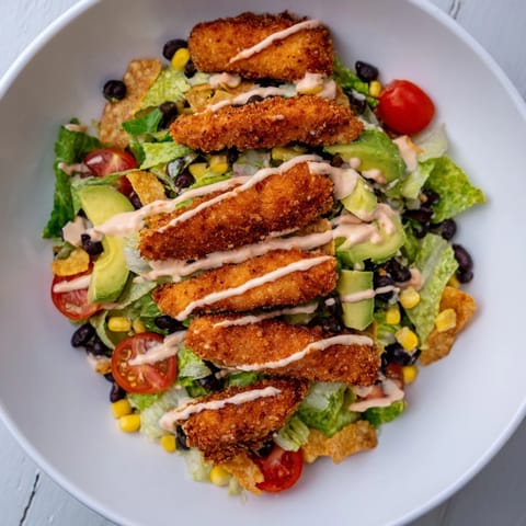 Fresh avocado, cherry tomatoes, and shredded cheddar cheese mingle with spiced chicken in this hearty Crispy Chicken Taco Salad for a quick Tex-Mex dinner.