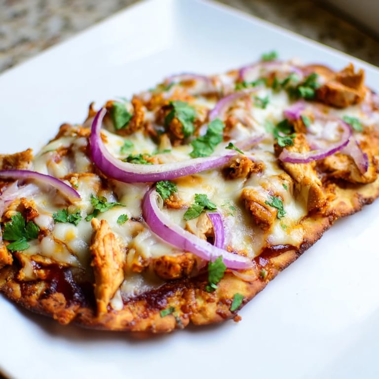 A slice of warm BBQ chicken flatbread being lifted, revealing the gooey mozzarella and savory grilled chicken, with fresh cilantro and sliced red onions on top.