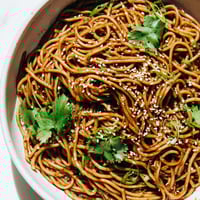 Chilled Spicy Sesame Noodle Salad garnished with fresh cucumbers, cilantro, and toasted peanuts on a platter.  