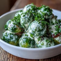 Golden-brown Brussels sprouts coated in a creamy Dijon mustard sauce, garnished with fresh parsley and served warm alongside roasted chicken.