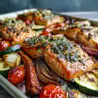 Golden-baked salmon fillets and colorful roasted vegetables from the Sheet Pan Salmon and Veggies Bowl, garnished with fresh parsley and lemon wedges on a rustic serving platter.