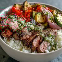 Freshly grilled steak slices rest on fluffy white rice with colorful roasted vegetables and chimichurri in a Grilled Steak Bowl.